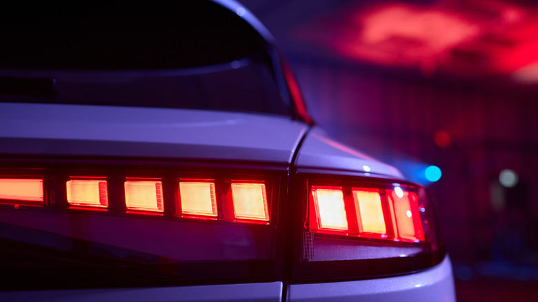 Close-up of a car's illuminated red brake lights in a dimly lit garage with purple and red lighting.