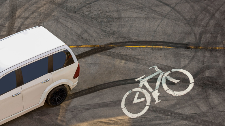 White SUV on an asphalt road with skid marks crossing over a painted bicycle lane symbol.