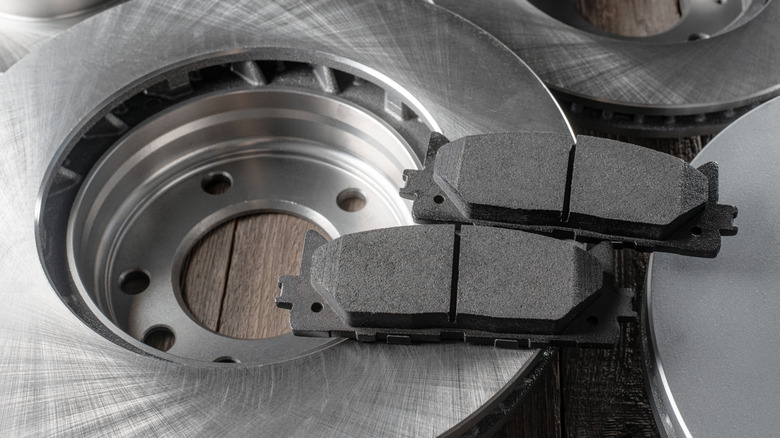 New brake pads resting on clean, unused brake rotors placed on a wooden surface in a workshop setting.