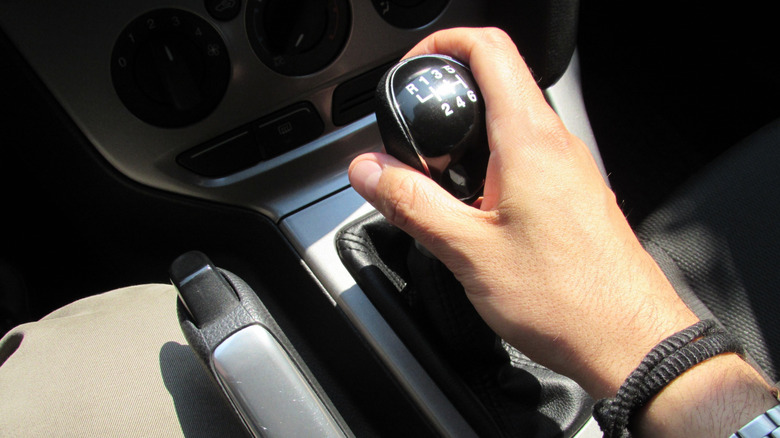 Driver's hand on a manual gear shift inside a car, preparing to change gears.