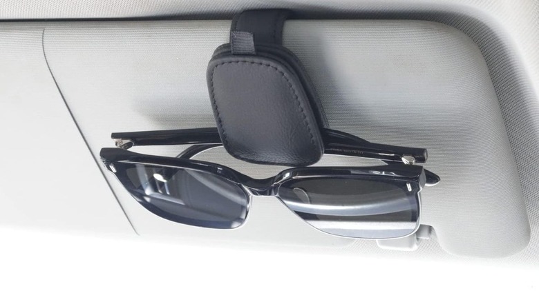 The Yuoyar sunglasses holder holding a pair of sunglasses, attached to the sun visor of a car