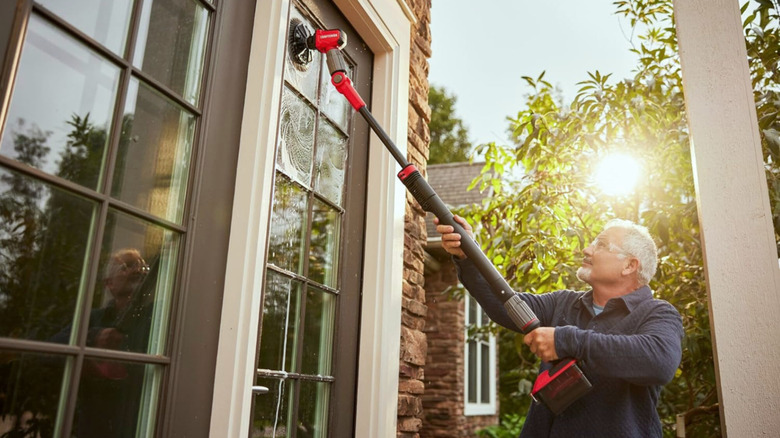 A man uses a pole power scrubber to clean a window outside a home during the day