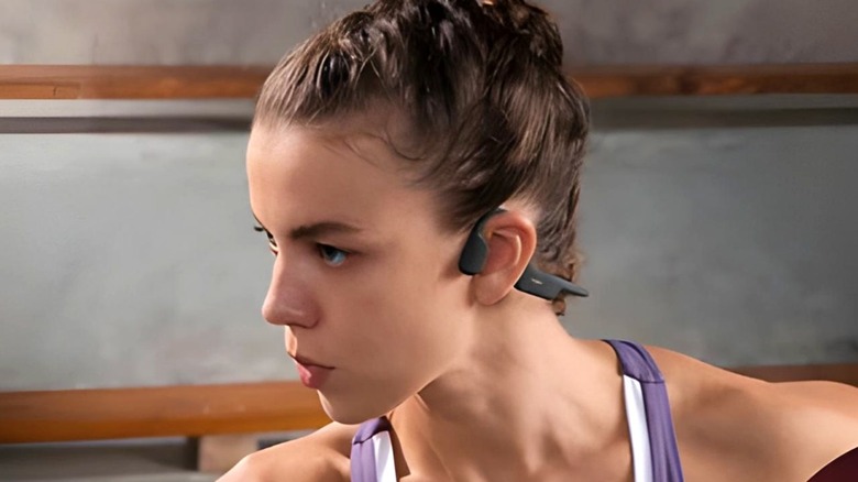 Woman in workout clothes wearing open ear earphones.