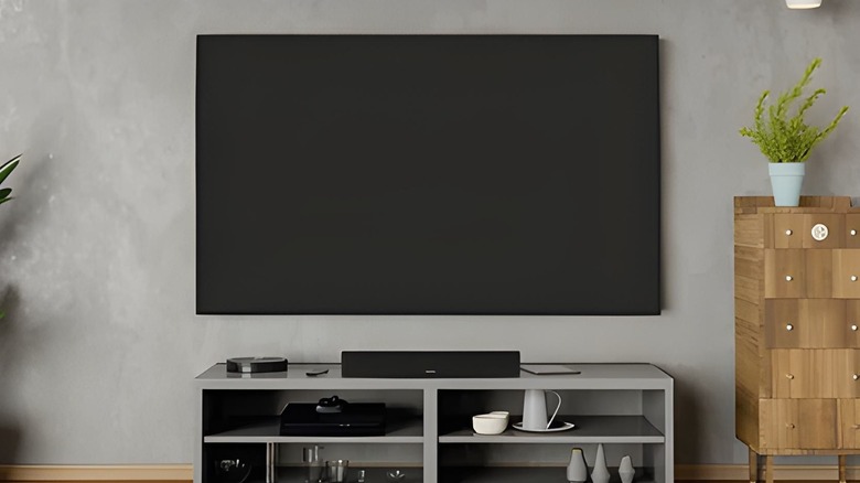 A Bose Soundbar on a TV stand, under a TV attached to the wall.