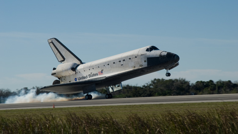 The space shuttle Atlantis touching down on the runway with smoke coming off the main gear tires while the nose gear tires are still in the air.