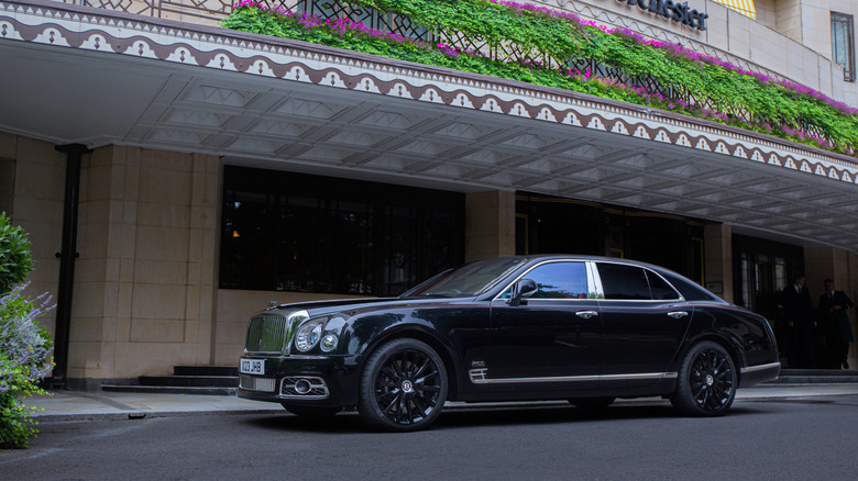 A black standard wheelbase Bentley Mulsanne parked in front of a branch of the Dorchester hotel.