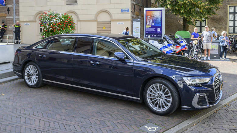A Black Audi A8 carrying the King of The Netherlands moving through a narrow road with a crowd in the back.