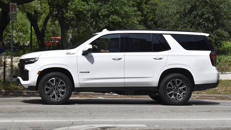 A white 2025 Chevrolet Tahoe parked at the side of a road, with trees visible in the back.