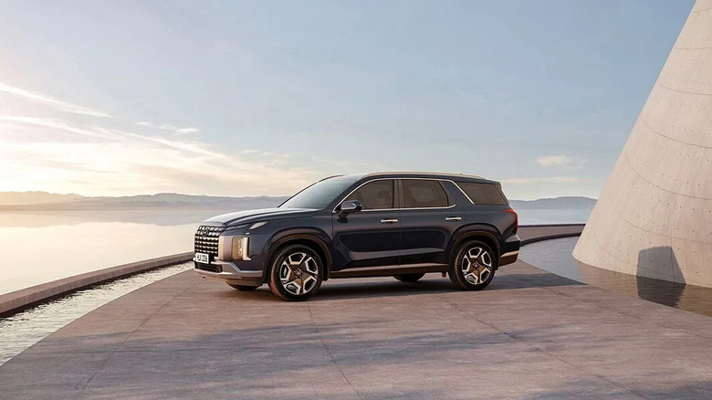 2025 Hyundai Palisade SUV parked on a modern, curved waterfront platform at sunset, with sleek architectural elements and a scenic horizon in the background.
