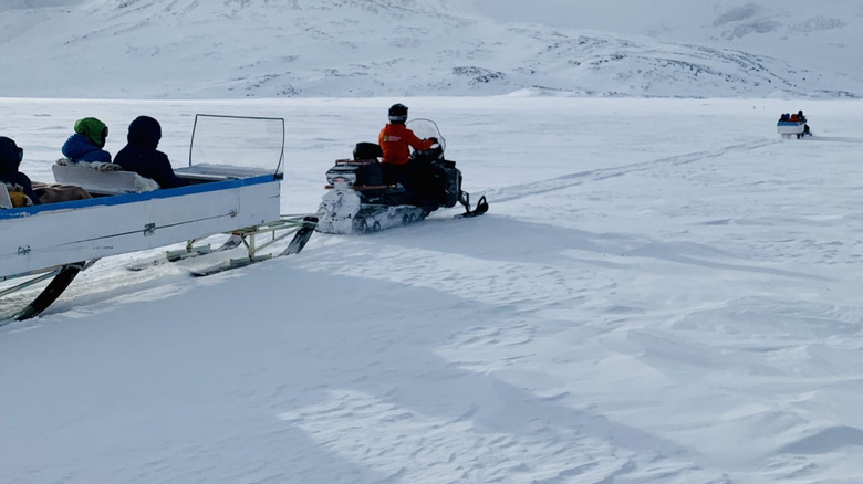 A sled holding three people that is being pulled by a snowmobile rider - one of many of the arctic region's snowmobile taxis in action.
