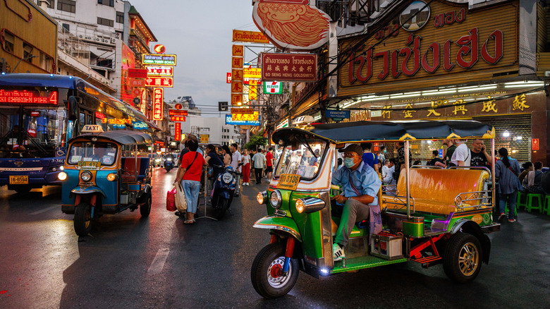 A brightly coloured tourist Tuk-Tuk driving along a busy main road in a city in Thailand