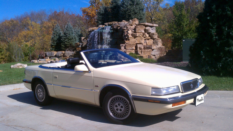 Beige 1990 Chrysler TC by Maserati convertible seen from right front parked in front of a waterfall feature