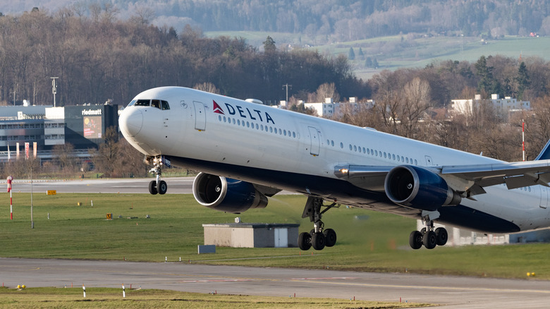 A Delta Airlines Boeing 767-400ER departing from a Switzerland airport, right to left, with trees and tarmac visible in the background.