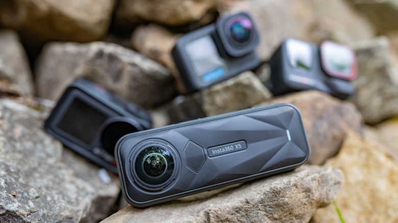 The Insta360 X5 with several out of focus action cameras in the background.