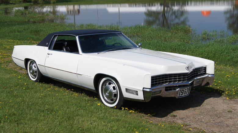 White 1967 Cadillac Eldorado with black roof and headlights hidden seen from right front by a pond