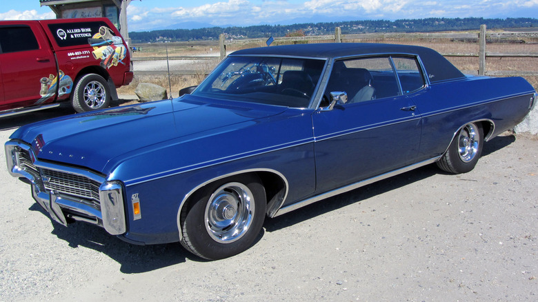 Blue 1969 Chevrolet Caprice coupe seen from left front parked in front of a fence and field