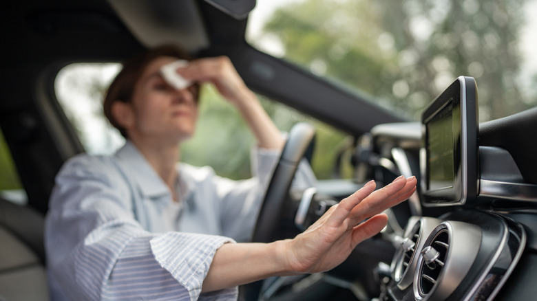 A person in the driver seats check the air conditioning with one hand and wipes the sweat off with the other.