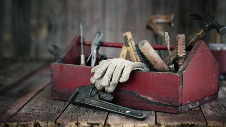 Antique work tools in a red toolbox on an old wood background