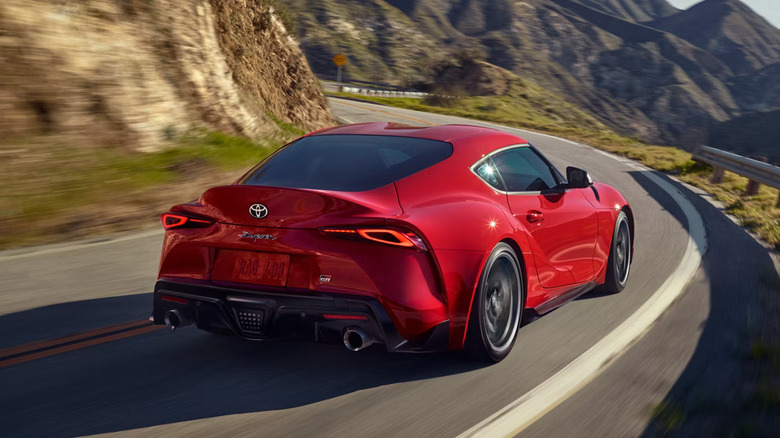 A red 2025 Toyota 3.0 Premium shown in Renaissance Red 2.0, zooming against a curving mountain road in the afternoon, rear view
