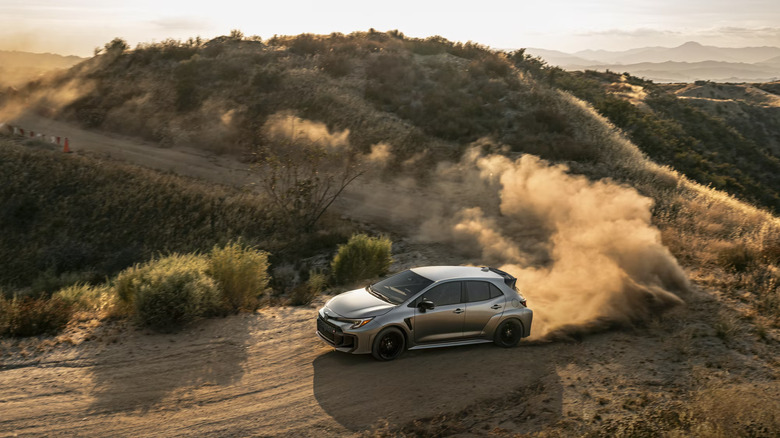 A silver Toyota GR Yaris taking a dusty corner at speed, arid vegetation visible in the background
