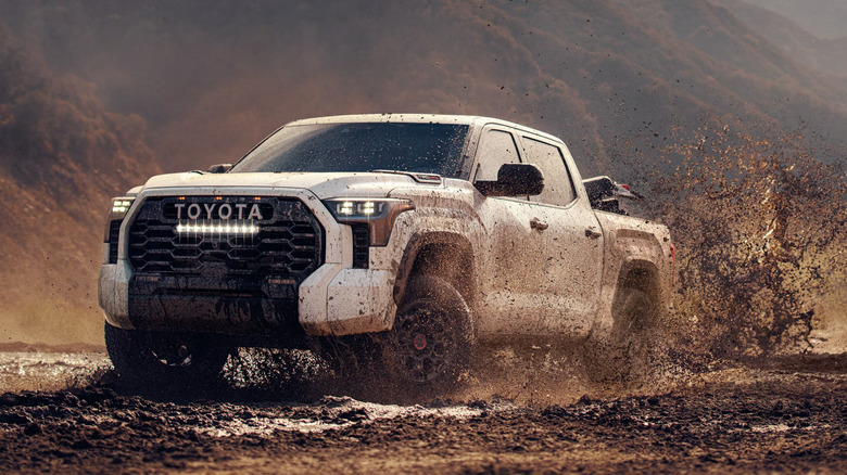 A white Toyota Tundra offroading in a muddy environment, front and left side views, kicking up mud