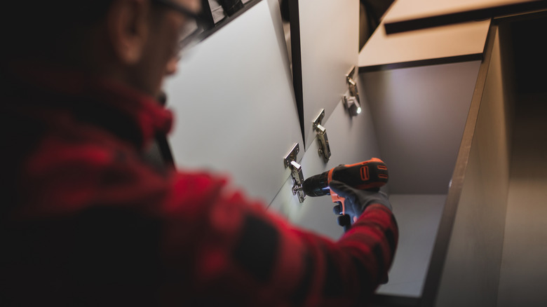 A person uses a small cordless drill to attach a screw to a piece of furniture