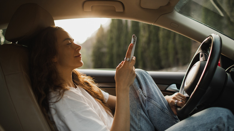 A driver scrolls on her phone while her car idles