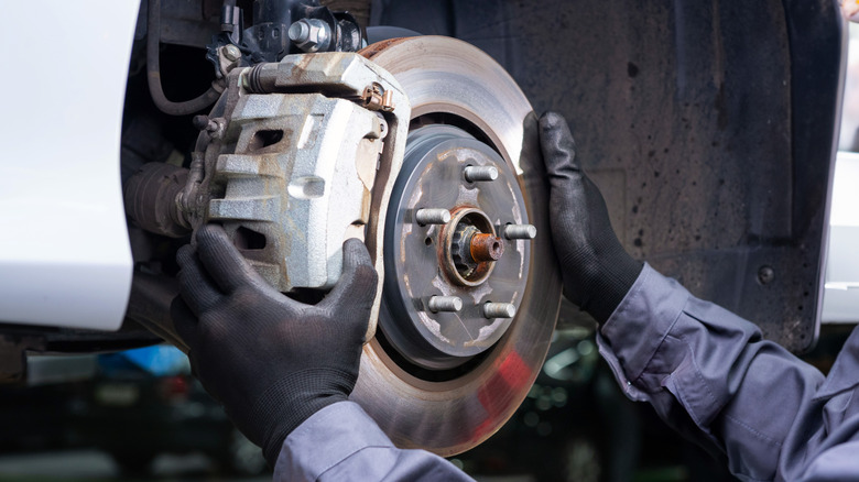 A mechanic with latex gloves working on the brake rotors of a car mounted on a jack