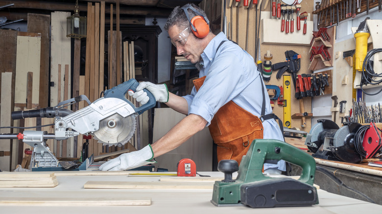 man wearing safety equipment while cutting a board