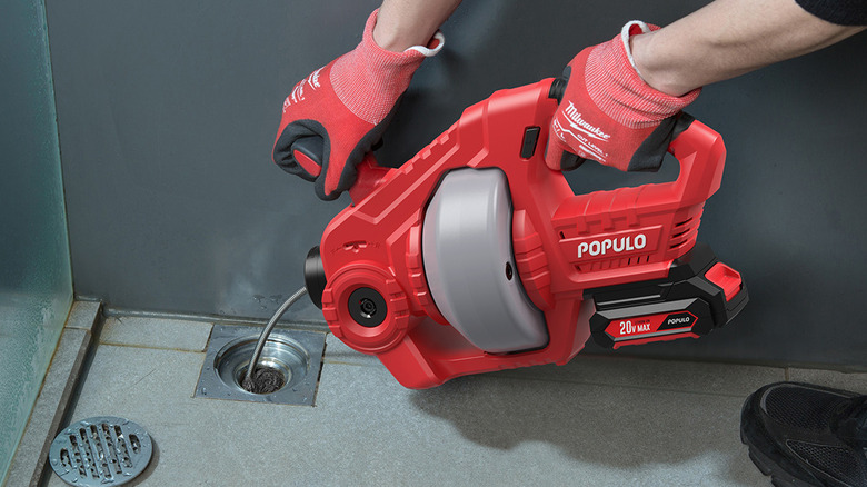 person using electric drain auger
