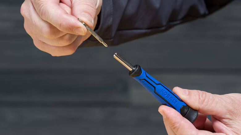 A man putting a screwdriver bit into a blue Kobalt screwdriver.