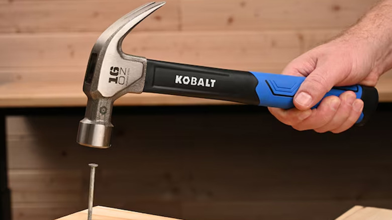A man hammering a nail into some wood with a standard claw hammer