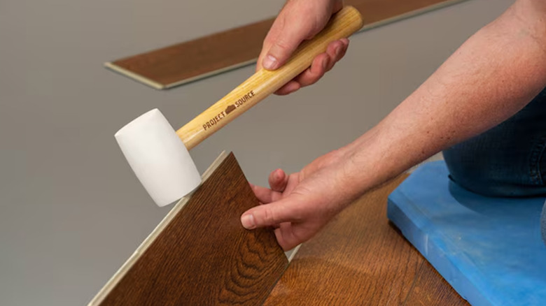 A man using a white rubber mallet on some flooring