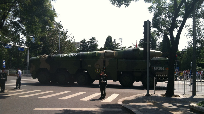 A Dongfeng 21 missile passing through a pedestrian crossingon the back of a truck while a crowd looks on.