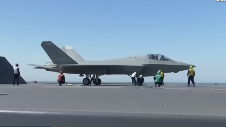 A grey Shenyang J-35 stealth fighter on the deck of a carrier, crew visible