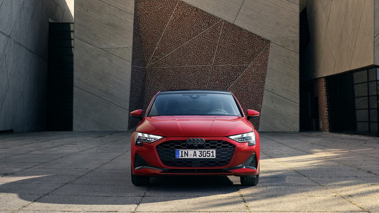 Front view of a red 2025 Audi A3 parked in front of a concrete building.