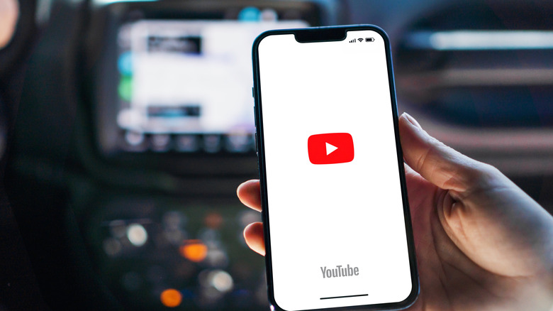 A girl opening the YouTube app on an iPhone with CarPlay running in the background