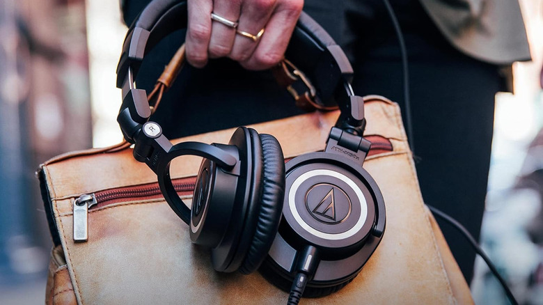 A person holding a bag and a pair of Audio-Technica ATH-M50x headphones.