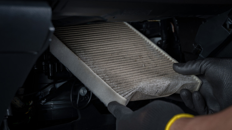 person removing dirty cabin air filter from vehicle