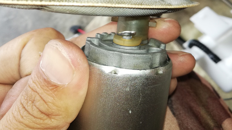 A person holding a fuel pump and sock, with the assembly in background