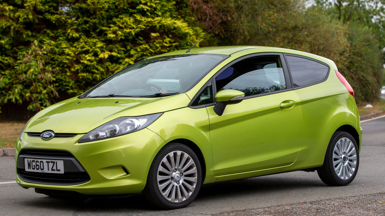 A neon green 2011 Ford Fiesta parked at the side of a street, trees in the back.