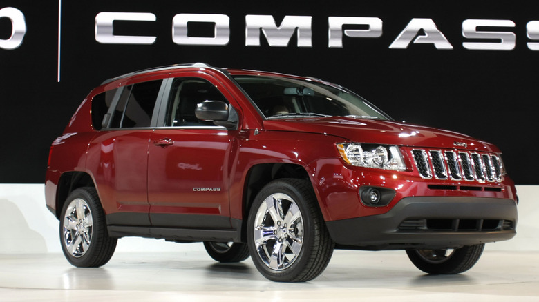 A red 2011 Jeep Compass on a podium with the Jeep logo on a wall at the back.