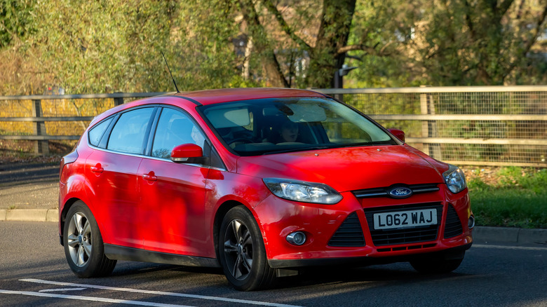 A dark red Ford Focus car with metallic pain driving down a shaded British road.