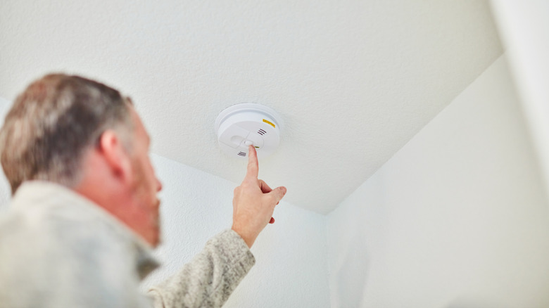 A man pressing the button on a smoke detector