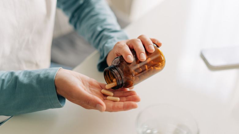 A person pouring capsules from a bottle into their open hand