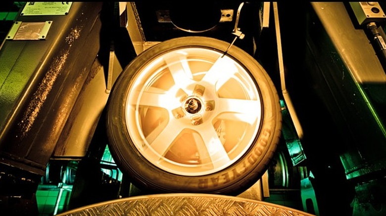 Tire spinning on testing equipment inside the Sava factory, with green and yellow lighting highlighting the machinery and motion blur showing rotation.