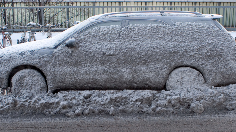 A parked station wagon is completely spattered in muddy snow