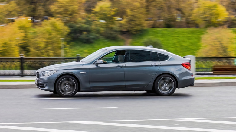 A BMW 5-series GT version driving from right to left with trees in the background