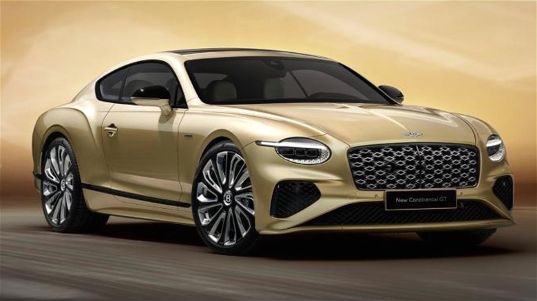 A 2026 gold Bentley Urban EV SUV is being unveiled in a showroom with a gold background.