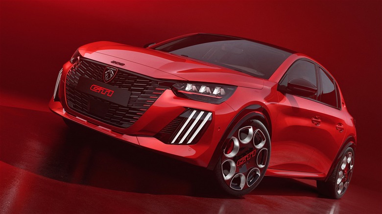 A bold red 2026 Peugeot e-208 GTi sits under dramatic studio lighting, showing off its aggressive front end, sporty wheels, and sharp LED headlights.
